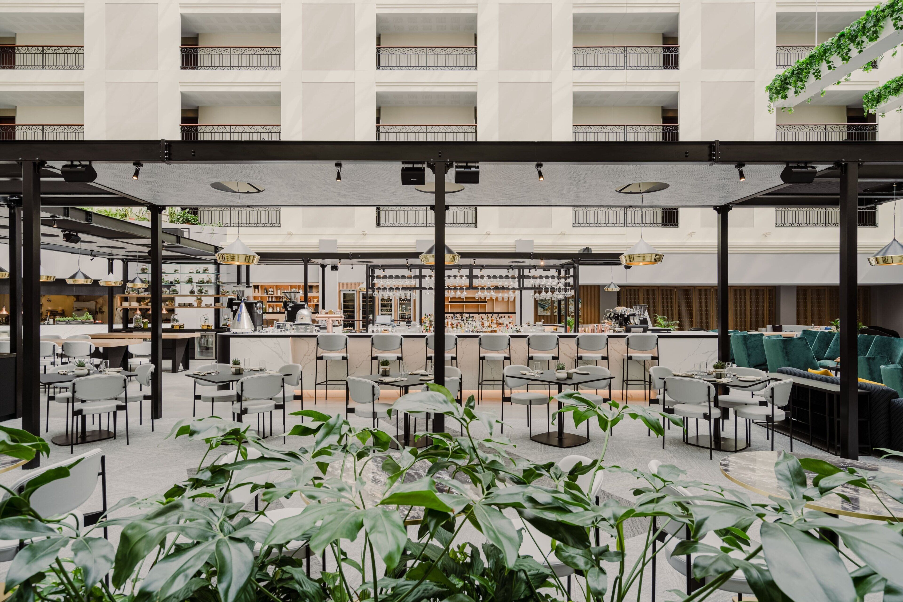 A spacious outdoor dining area with multiple tables and chairs, surrounded by large potted plants.