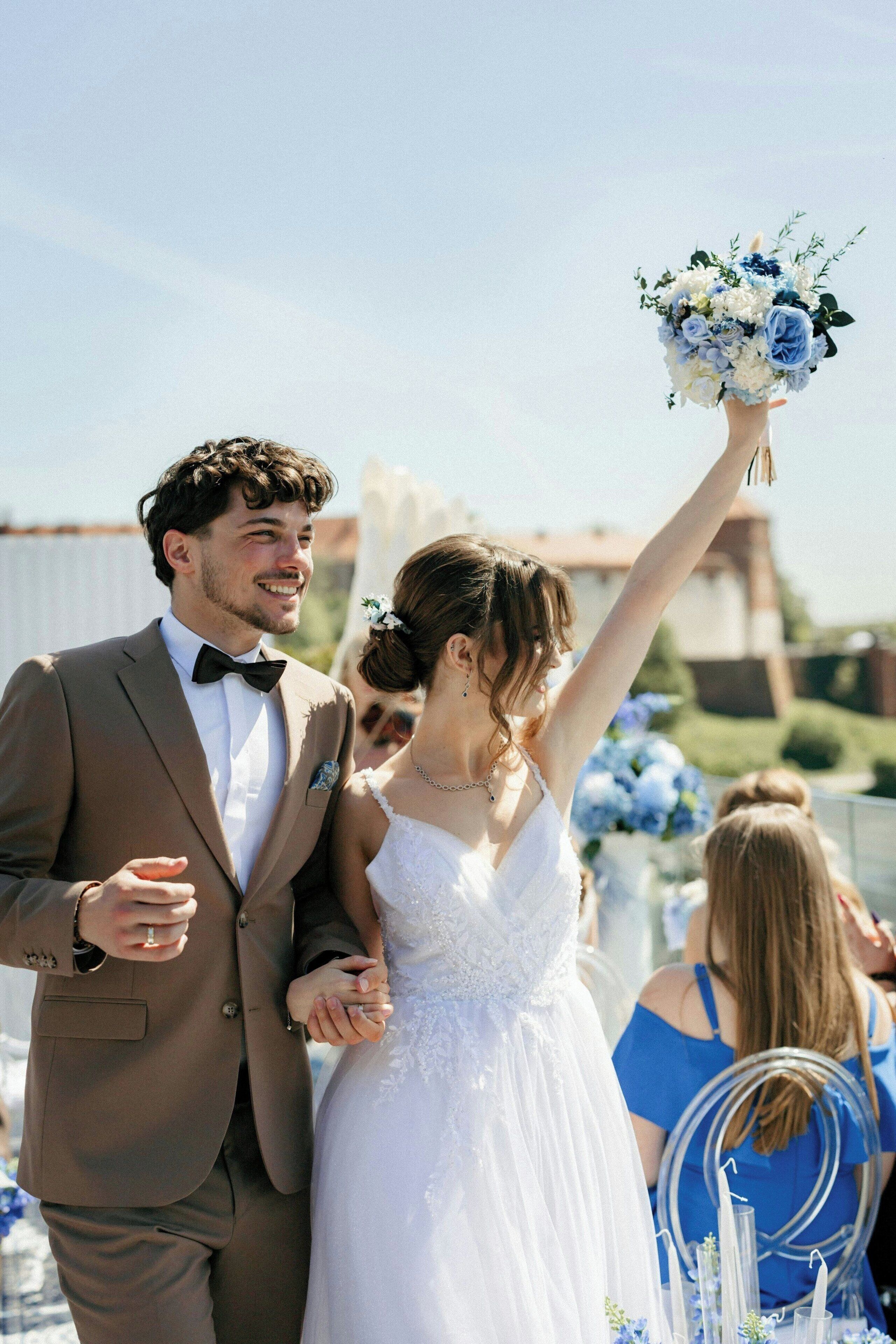 A wedding ceremony with a couple holding hands, a bride in a white dress, and a groom in a brown suit.