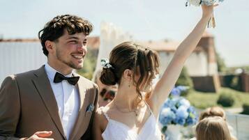 A wedding ceremony with a couple holding hands, a bride in a white dress, and a groom in a brown suit.
