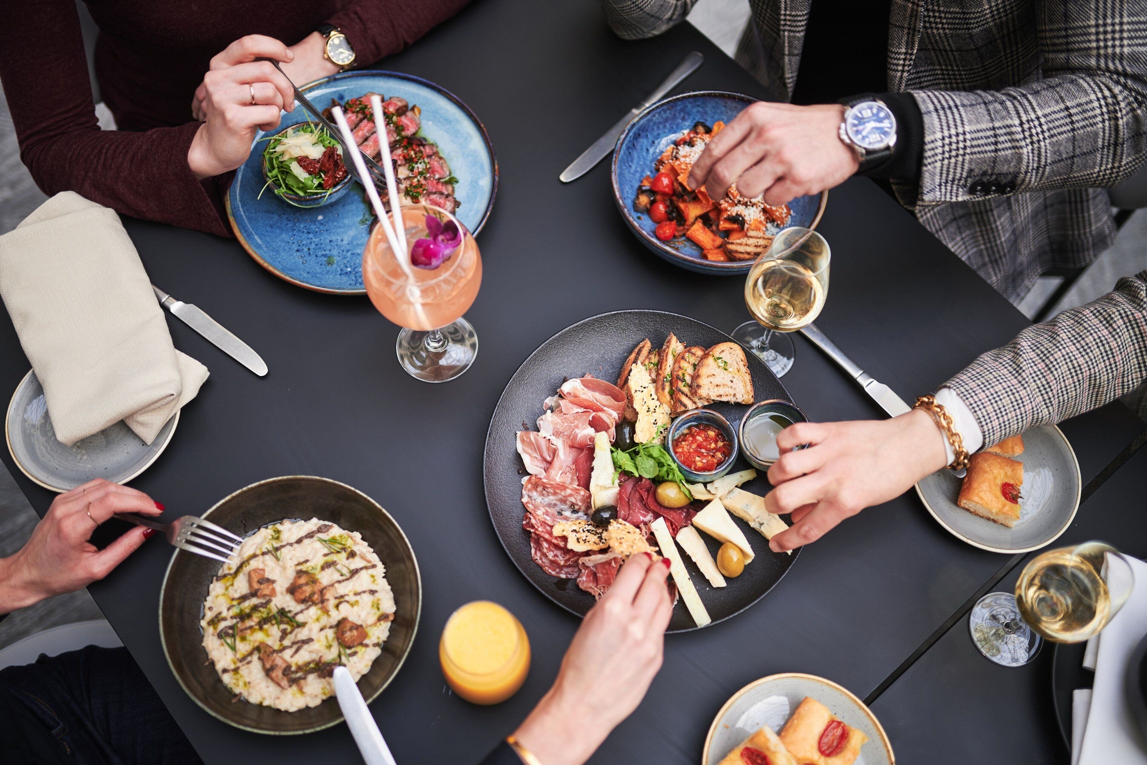 A group of people dining at a table with various dishes, including salads, meats, and bread.