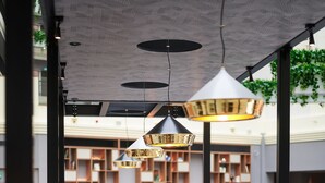 An indoor seating area with round tables and chairs, a patterned ceiling, and a view of a library in the background. - Sheraton Grand Krakow (Kraków)