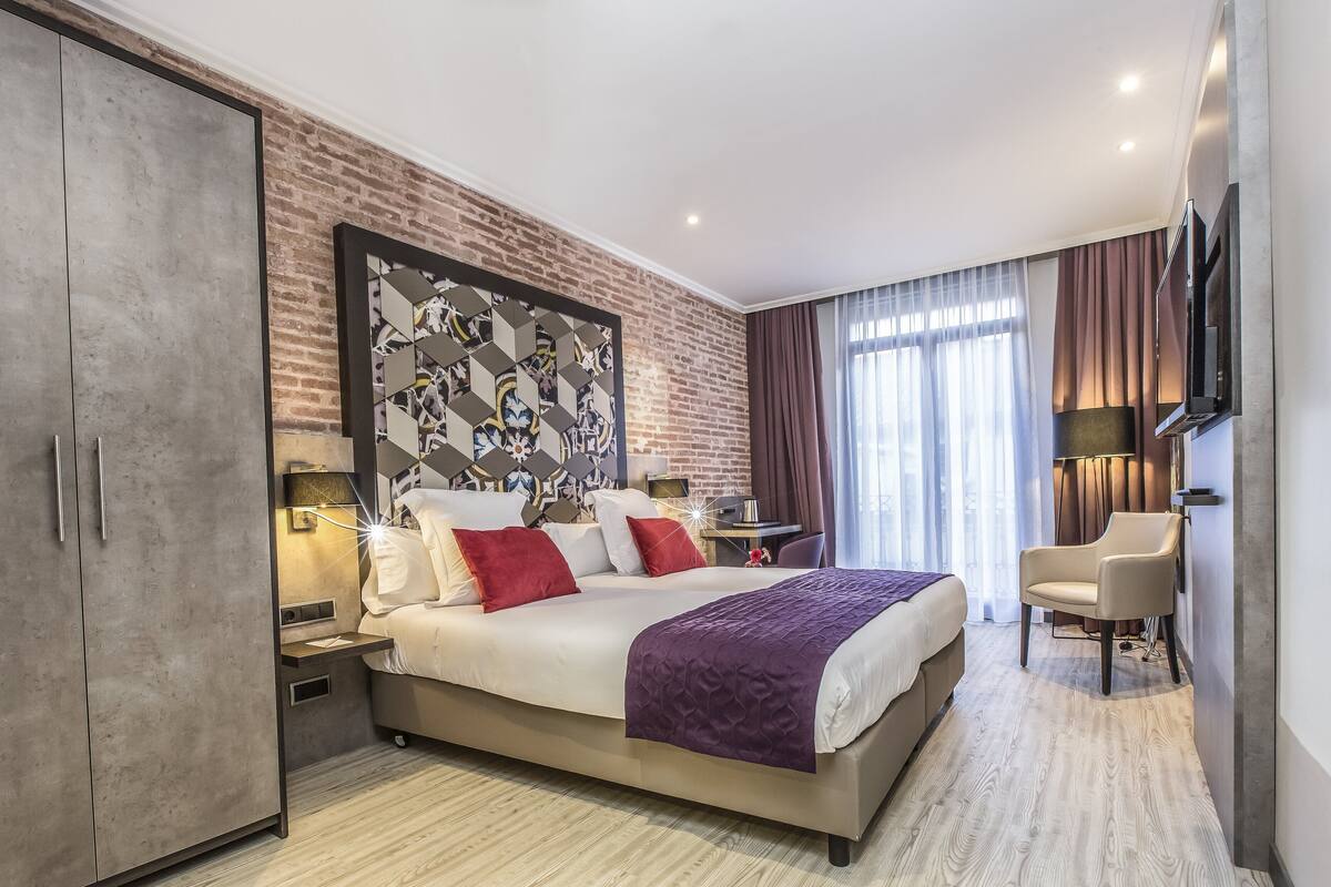 Moderni hotellihuone, jossa on suuri sänky, vaatekaappi, työpöytä ja televisio.