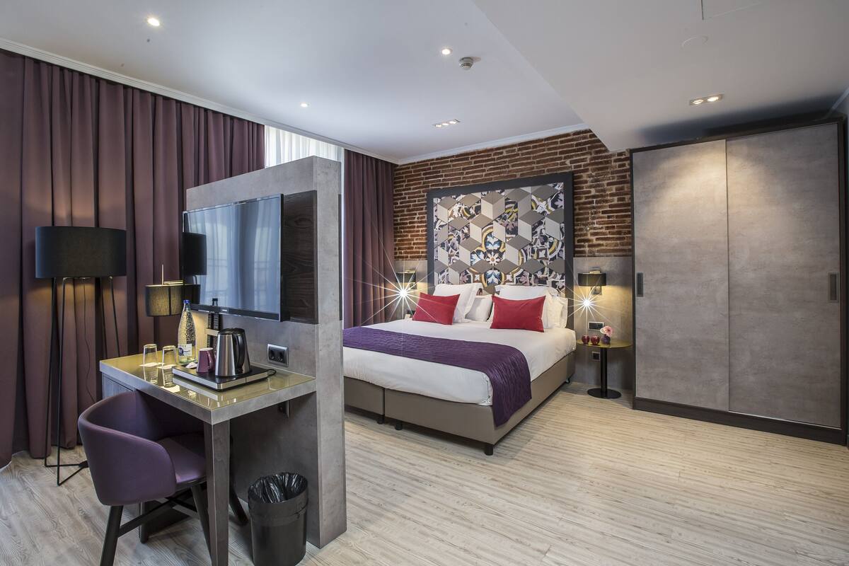 Moderni hotellihuone, jossa on sänky, työpöytä, tuoli, televisio ja vaatekaappi.