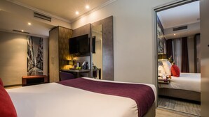 Hotellihuone, jossa on suuri sänky, työpöytä tuolilla, televisio ja peili.