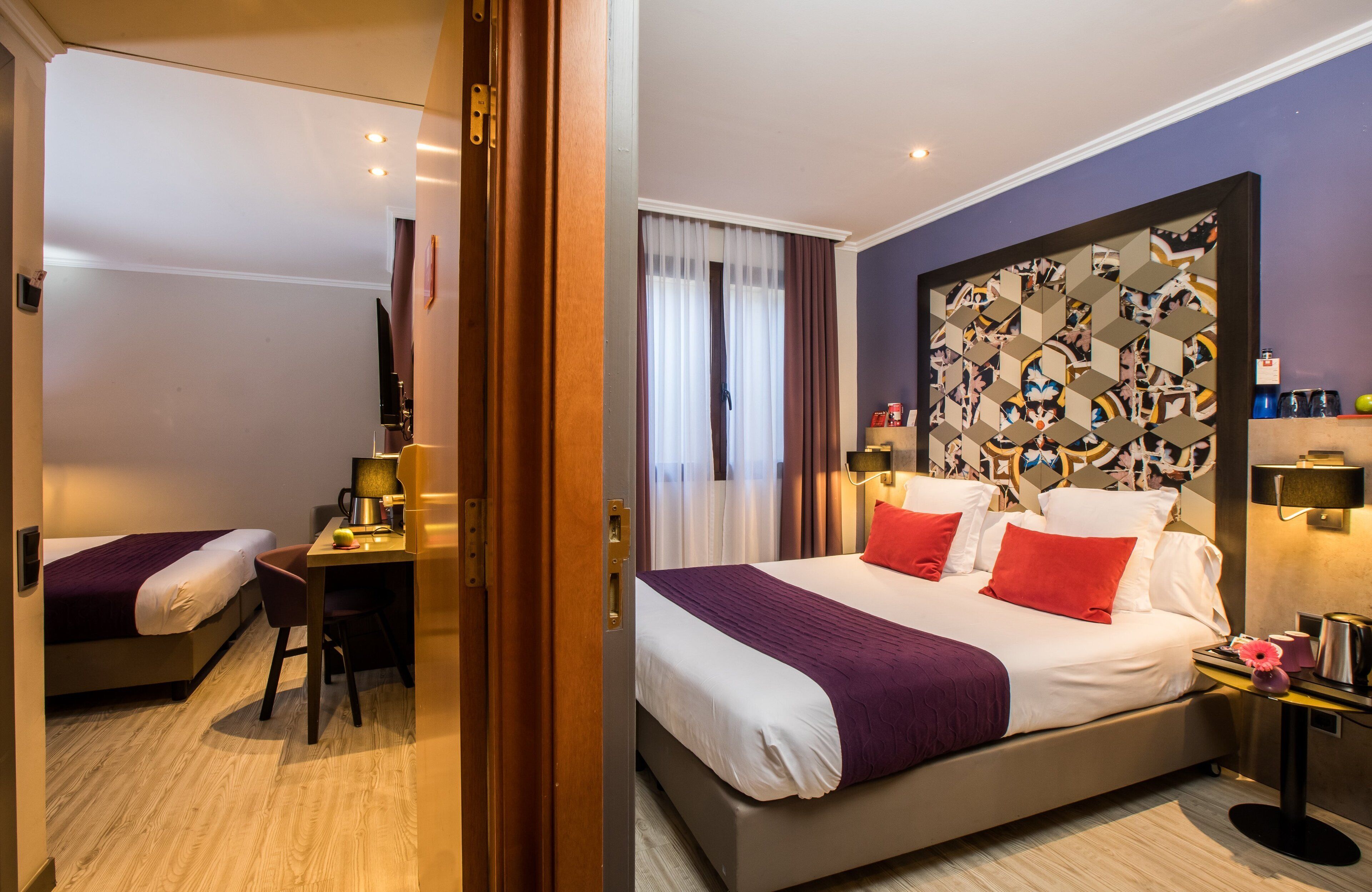 A hotel room with a bed, a desk, a chair, a coffee maker, and a nightstand with a lamp.
