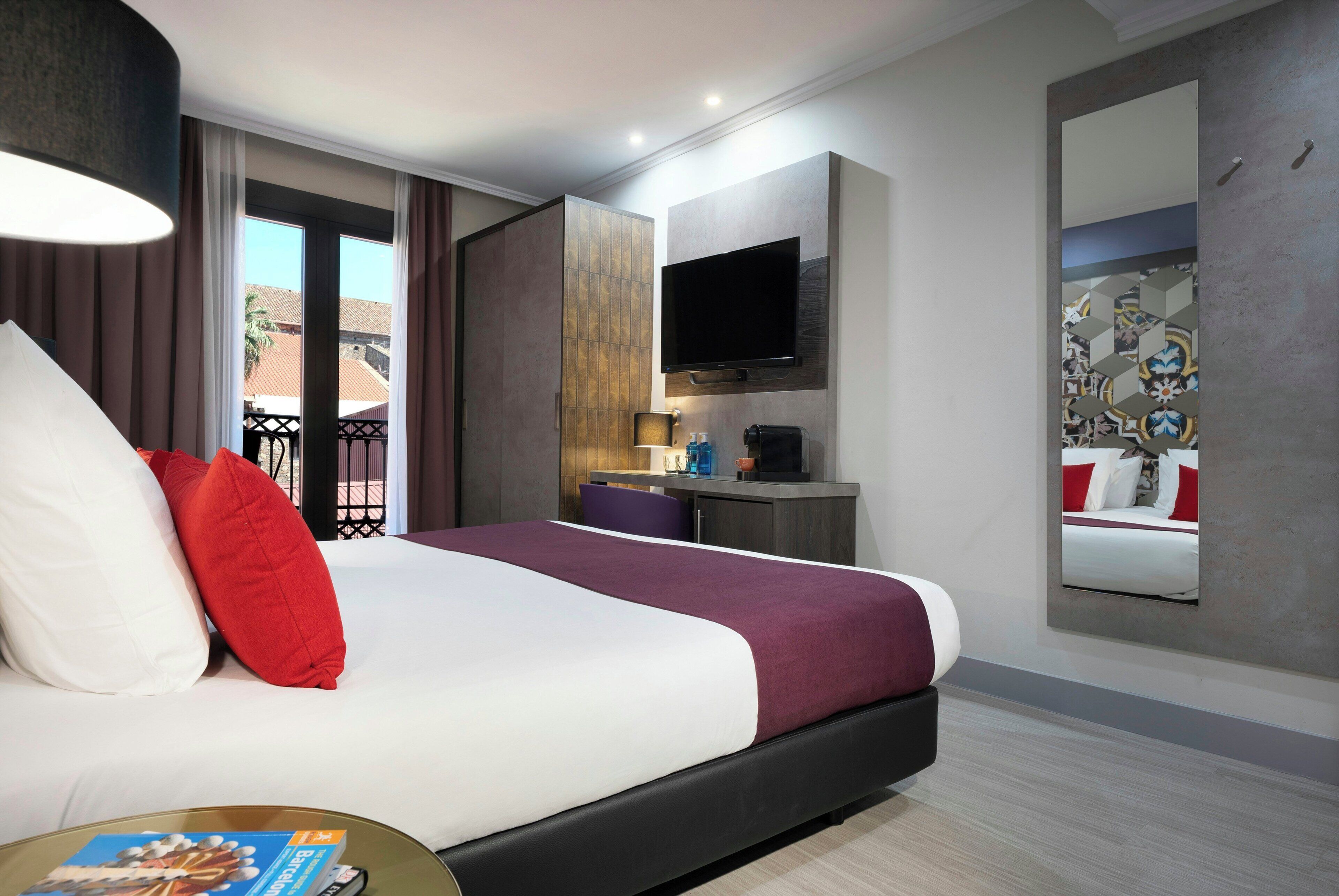 A hotel room with a bed, a television, a small table, and a window with curtains.