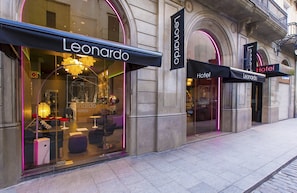 A hotel facade with 'Leonardo Hotels' signage, large arched windows, and a modern interior design visible through the glass.