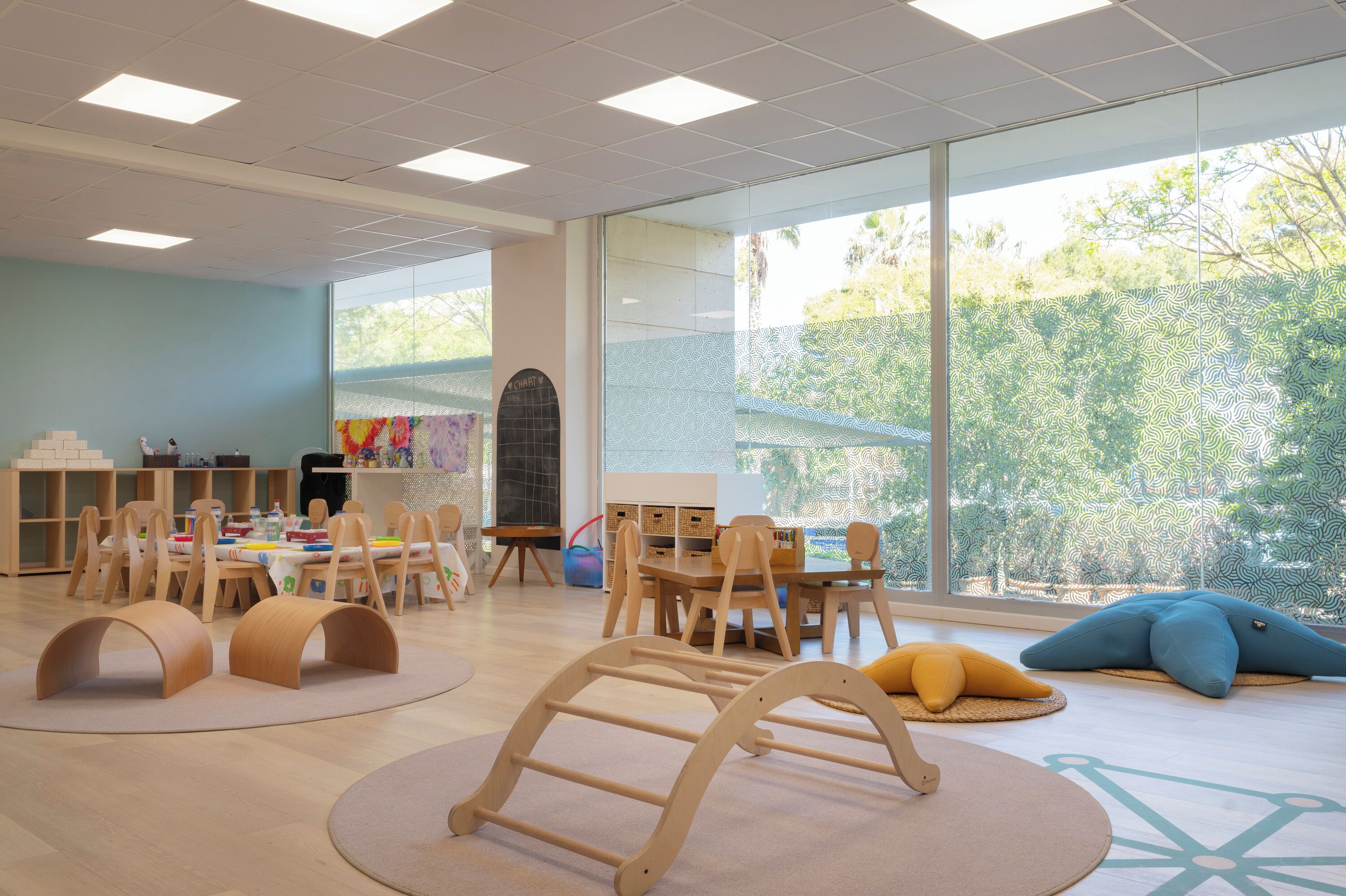 A spacious room with large windows, wooden furniture, and a play area.