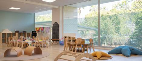 A spacious room with large windows, wooden furniture, and a play area.