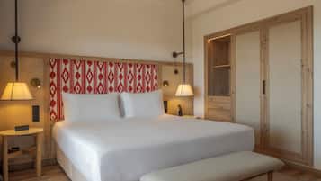 Una habitación de hotel con una cama grande, lámparas de noche, un armario de madera y un banco.