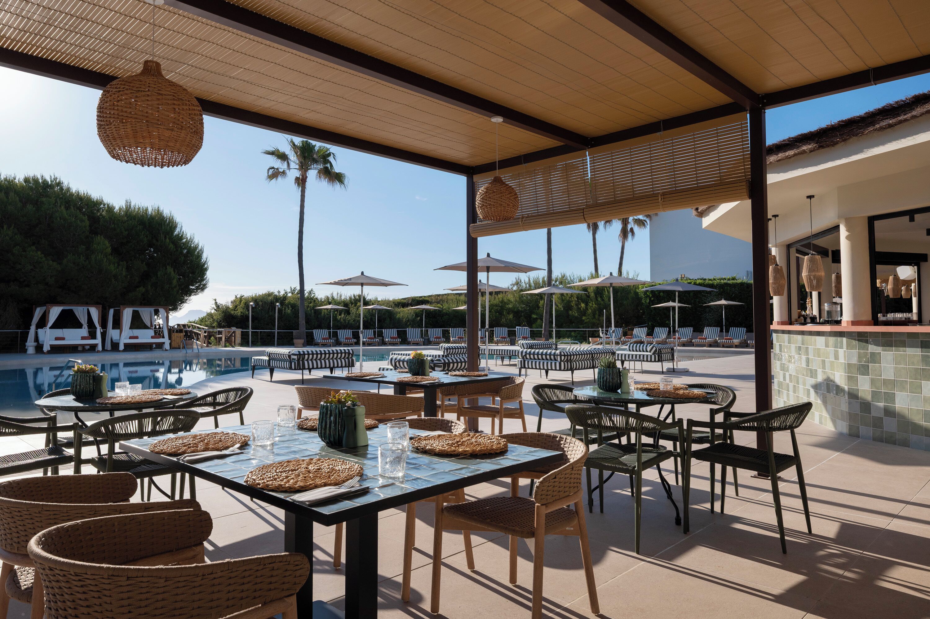 An outdoor dining area with tables and chairs, a pool, umbrellas, and lounge chairs.