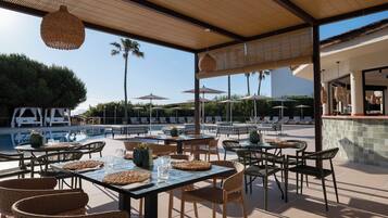 An outdoor dining area with tables and chairs, a pool, umbrellas, and lounge chairs.