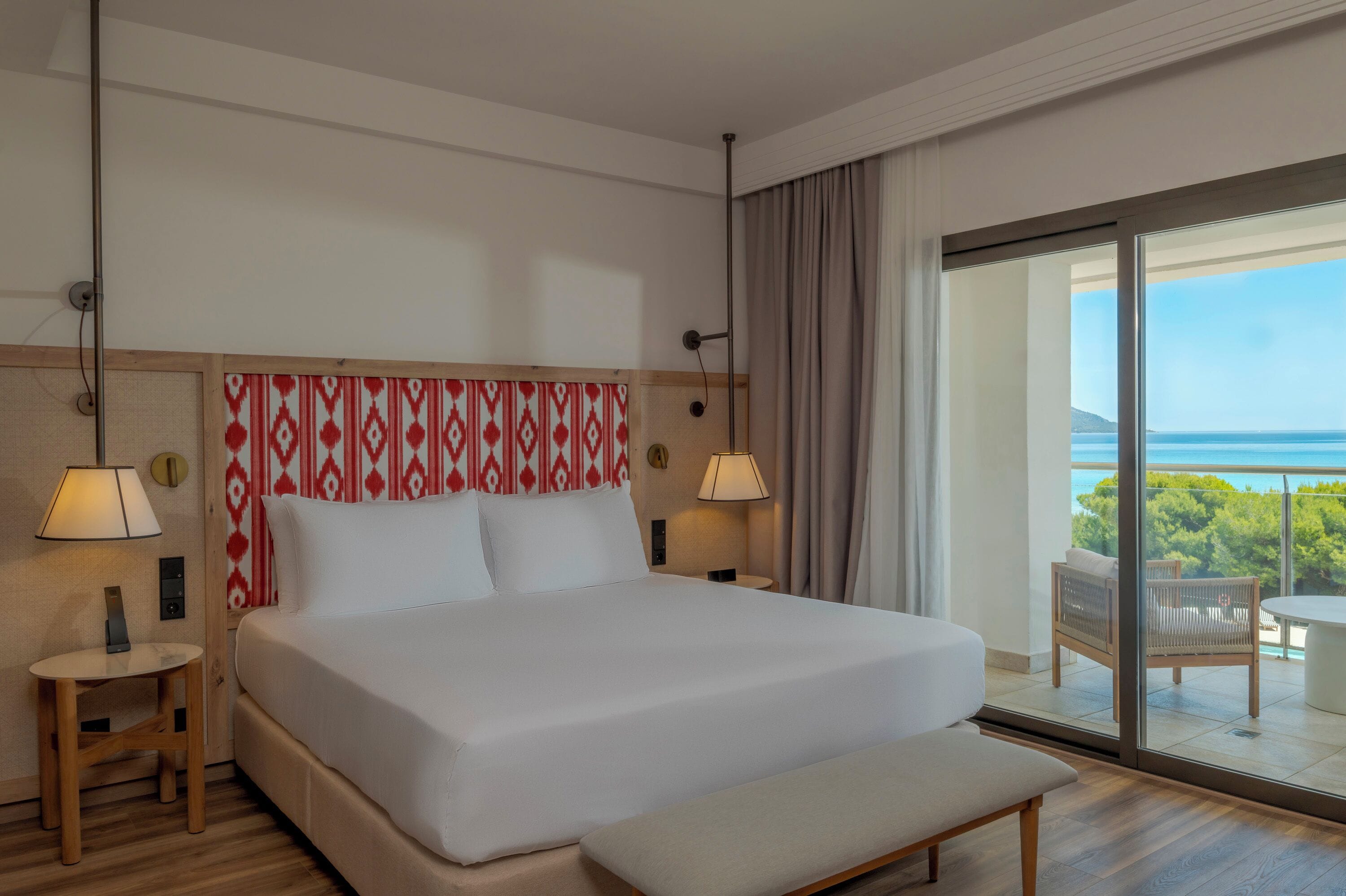 Une chambre d’hôtel avec un grand lit, des lampes de chevet, une petite table et un balcon donnant sur la mer.