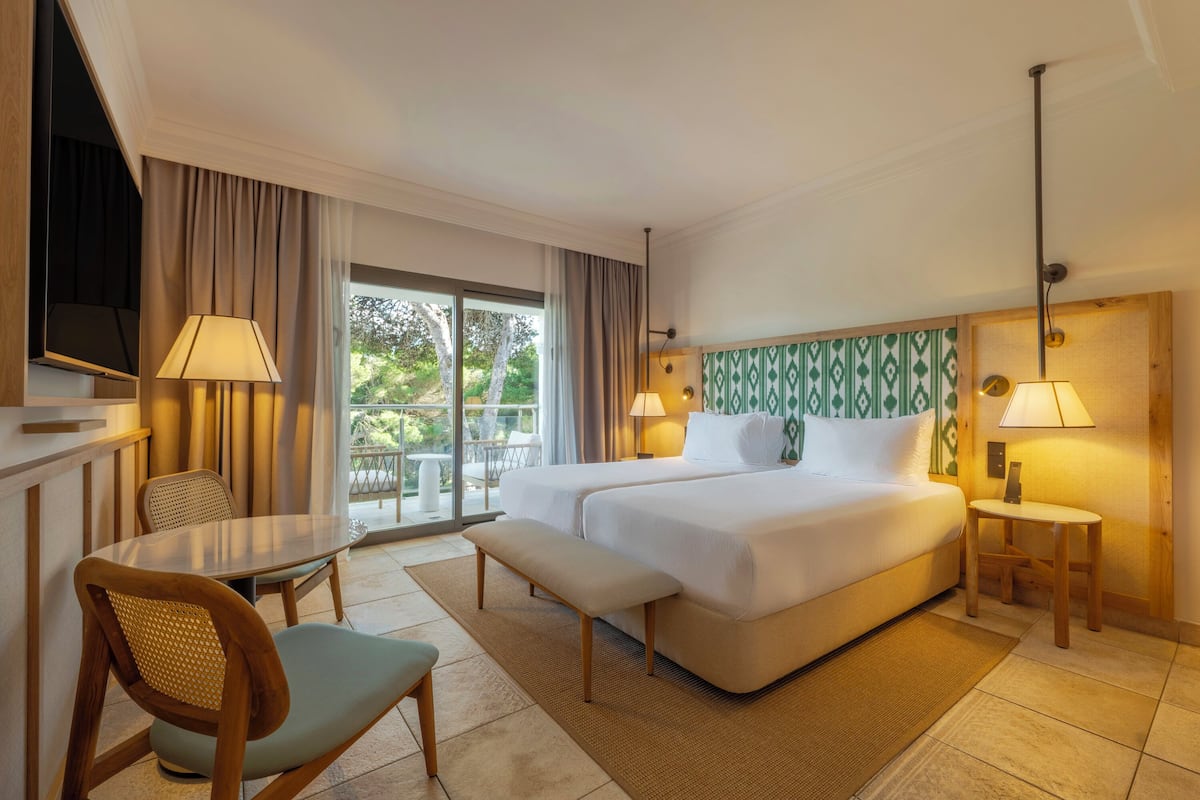 Habitación de hotel con cama, dos lámparas de noche, televisión, mesa de comedor con sillas y vistas al exterior.