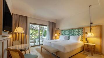 Habitación de hotel con cama, dos lámparas de noche, televisión, mesa de comedor con sillas y vistas al exterior.