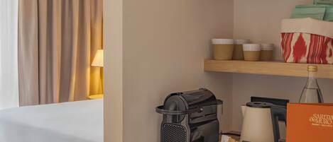 Habitación de hotel con cama, cafetera, una botella y una caja de palitos de pan.