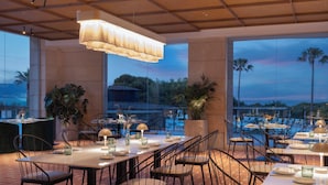 Un restaurante con terraza, ventanas amplias y vistas a palmeras y una piscina.