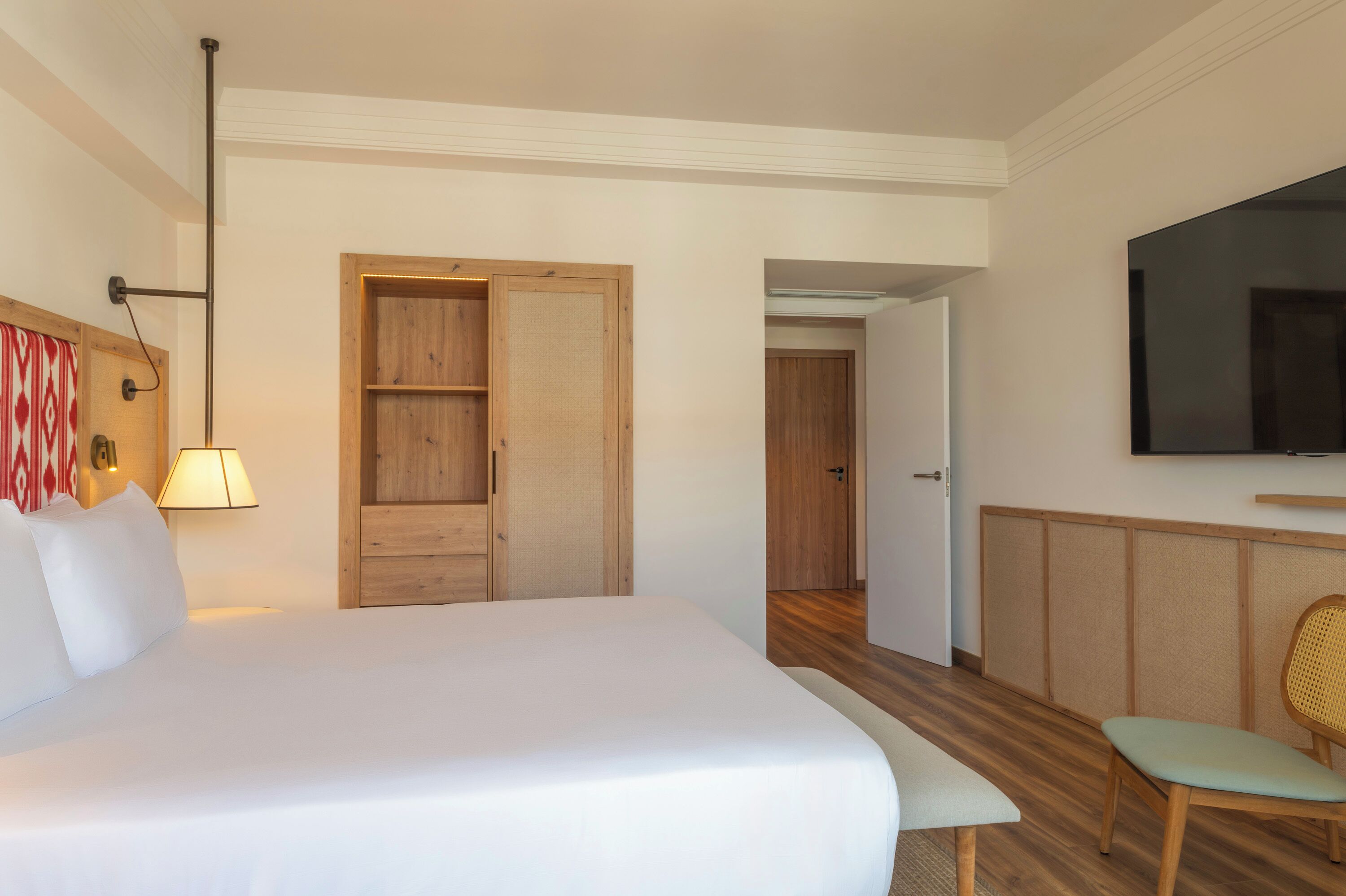Ein Hotelzimmer mit Bett, Schreibtisch, Stuhl, Fernseher, Kleiderschrank und einer Tür zu einem weiteren Raum.