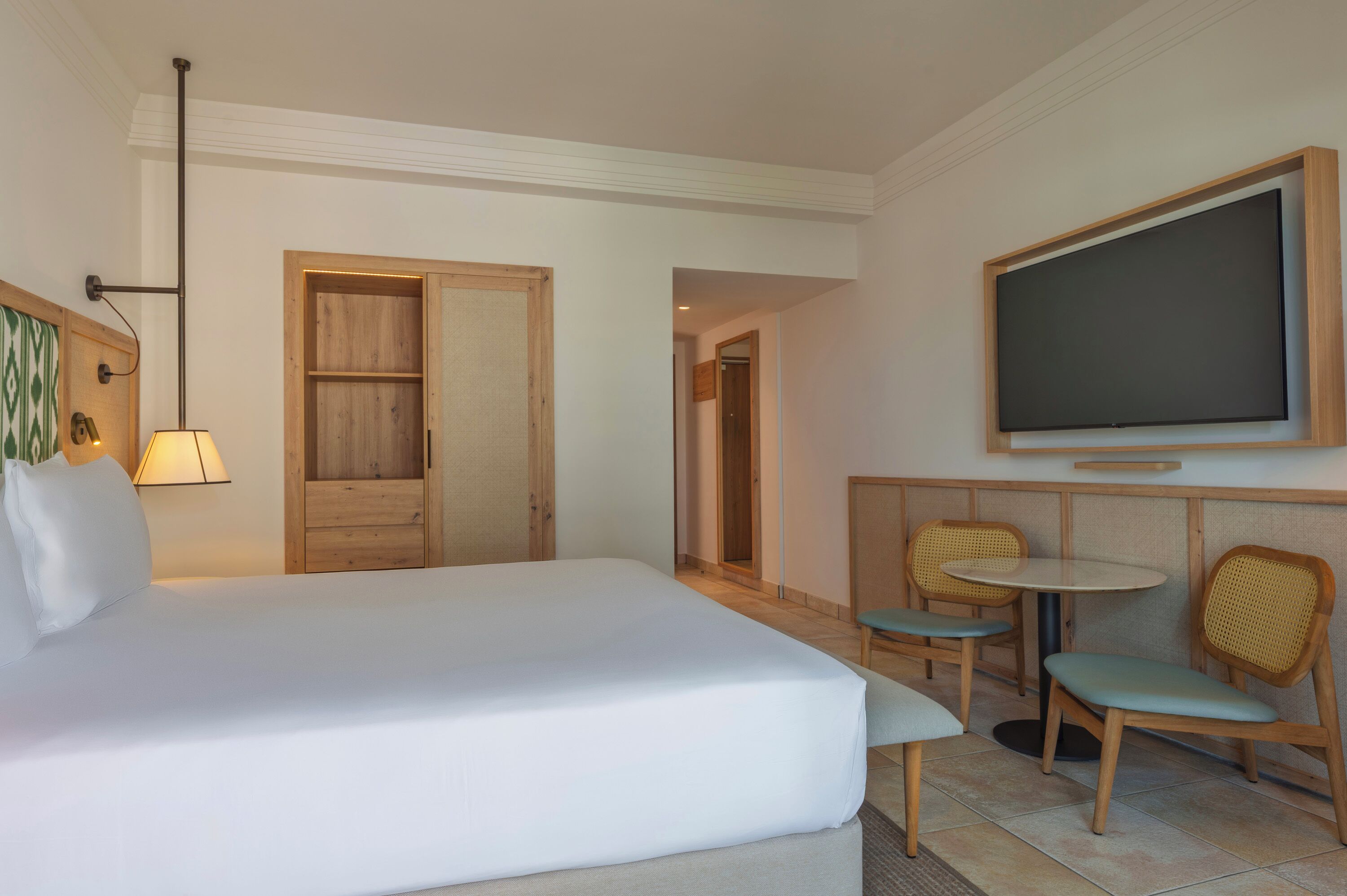 Ein Hotelzimmer mit Bett, Fernseher, kleinem Tisch, zwei Stühlen und einer Holztür.