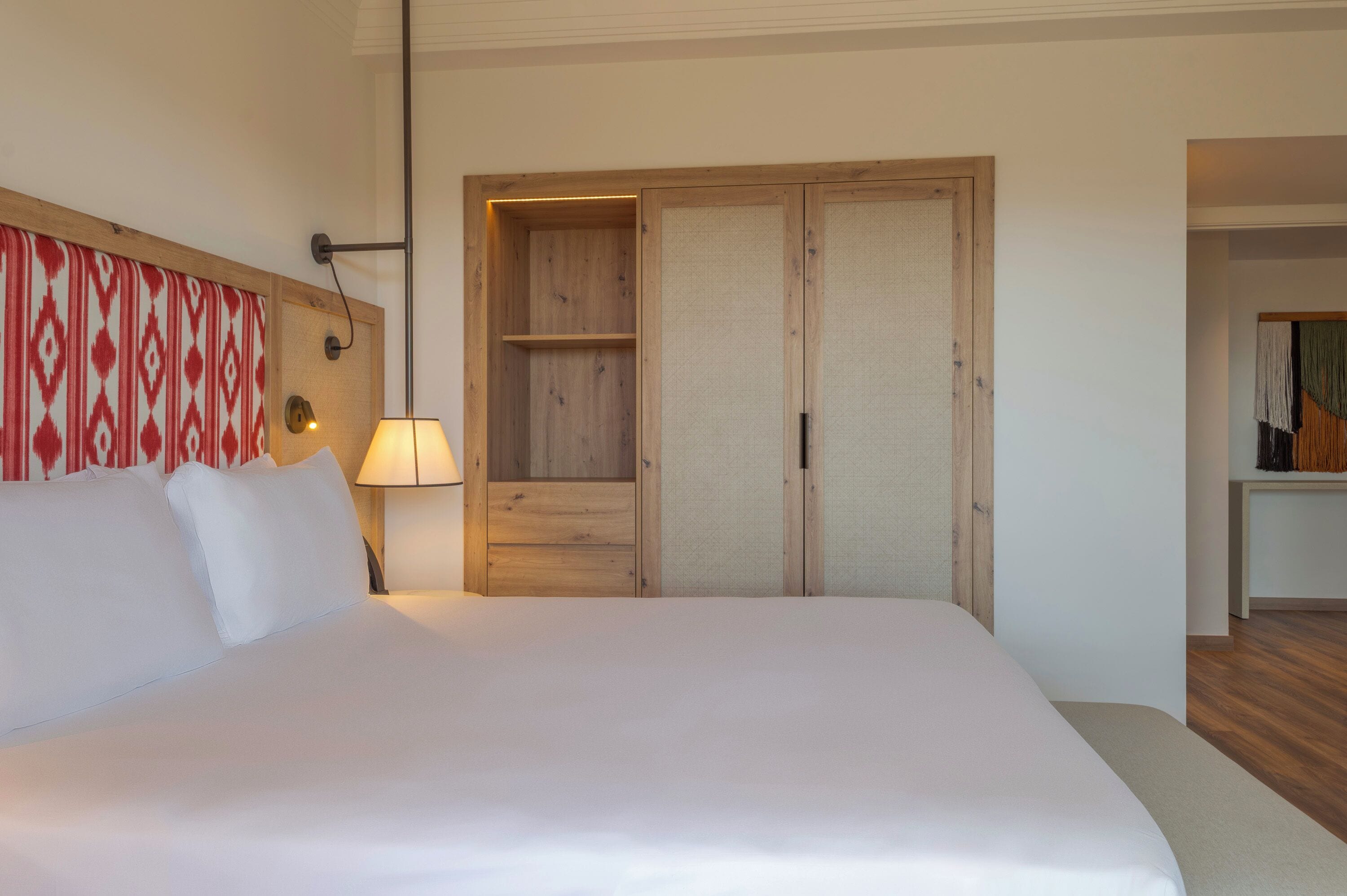 Una habitación de hotel con una cama grande, un armario de madera, una lámpara de noche y una cortina estampada.