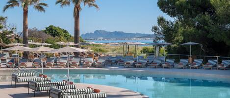 A poolside area with lounge chairs, umbrellas, and palm trees.