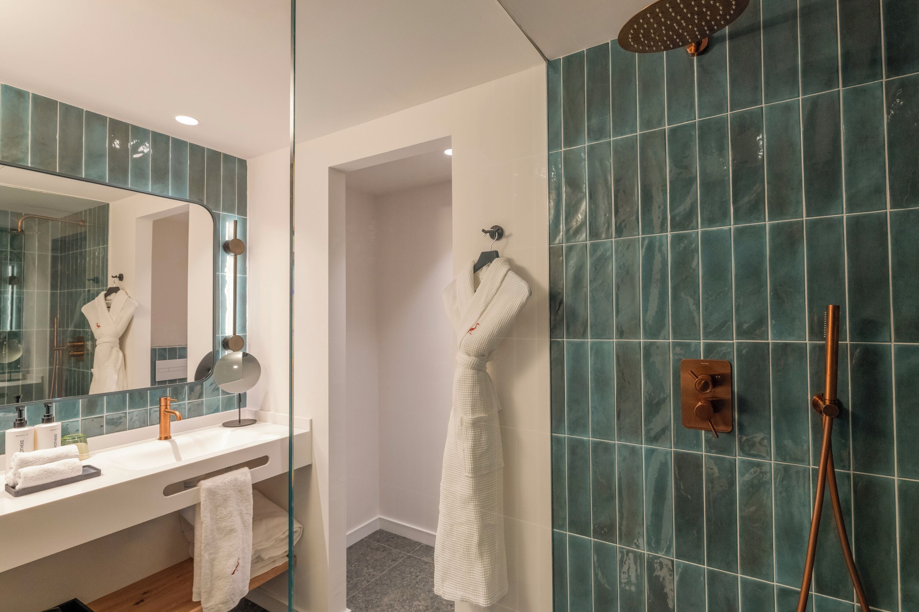 A modern bathroom with a large mirror, a white towel rack, a shower with a handheld showerhead, and a tiled wall.