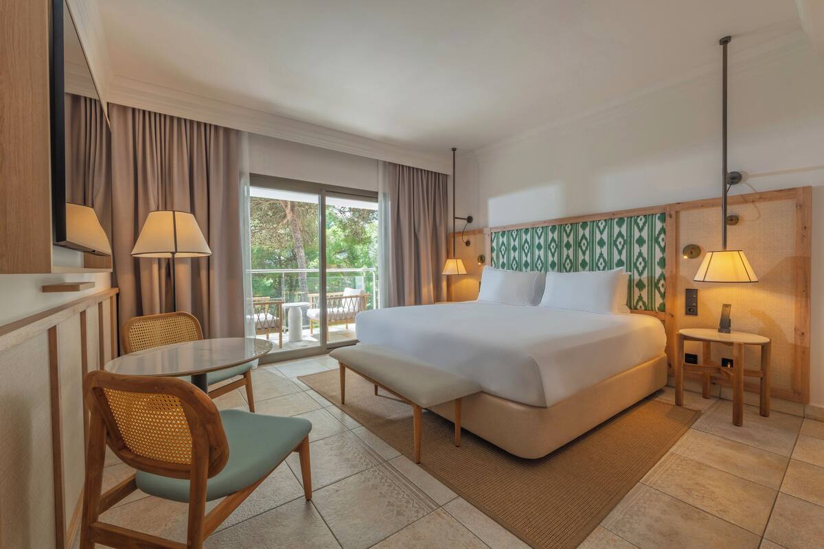 Habitación de hotel con cama, una mesa, una silla, un banco y vistas al exterior.