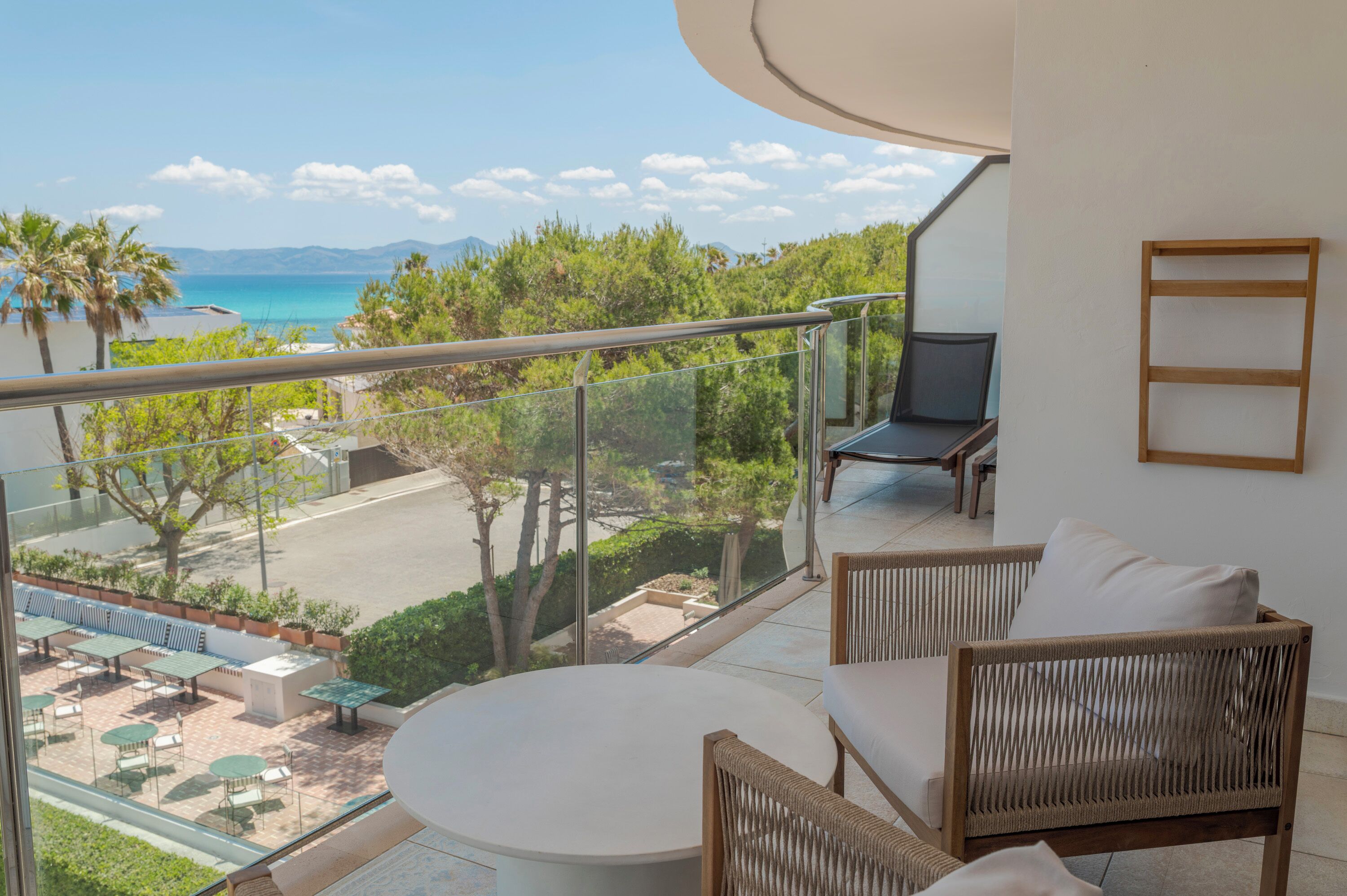 A balcony with a view of the sea, wicker furniture, and a glass railing.