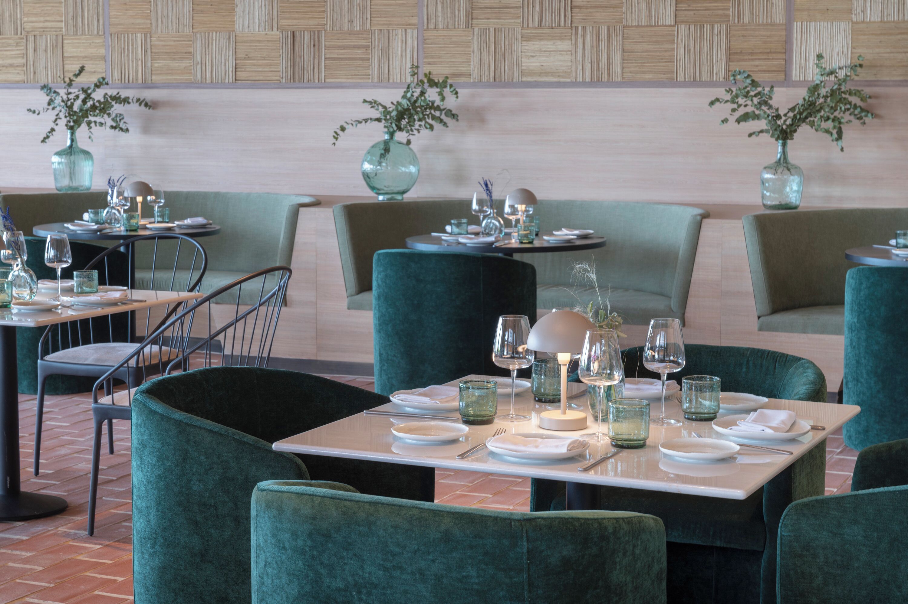A restaurant with green upholstered chairs, white table settings, and decorative vases on the tables.