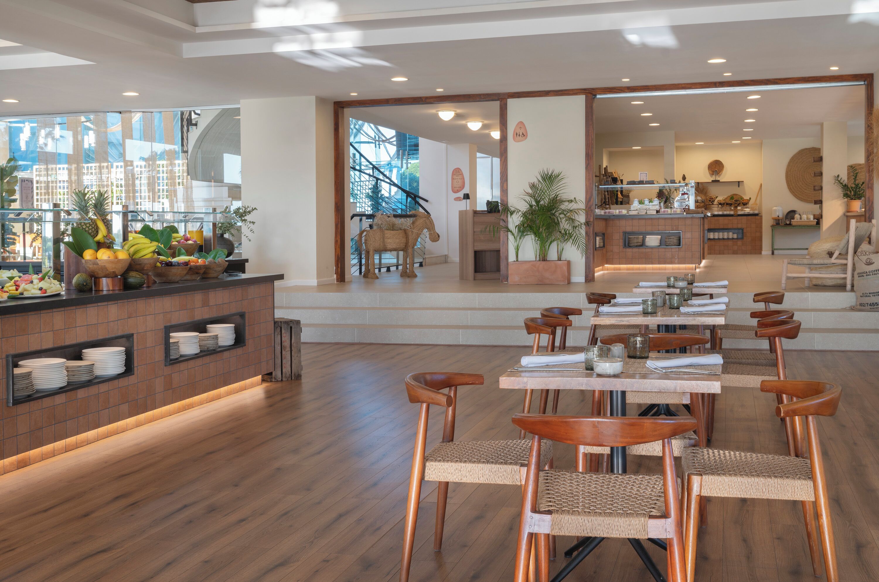 A modern restaurant with wooden floors, a fruit display, and a view of buildings through large windows.