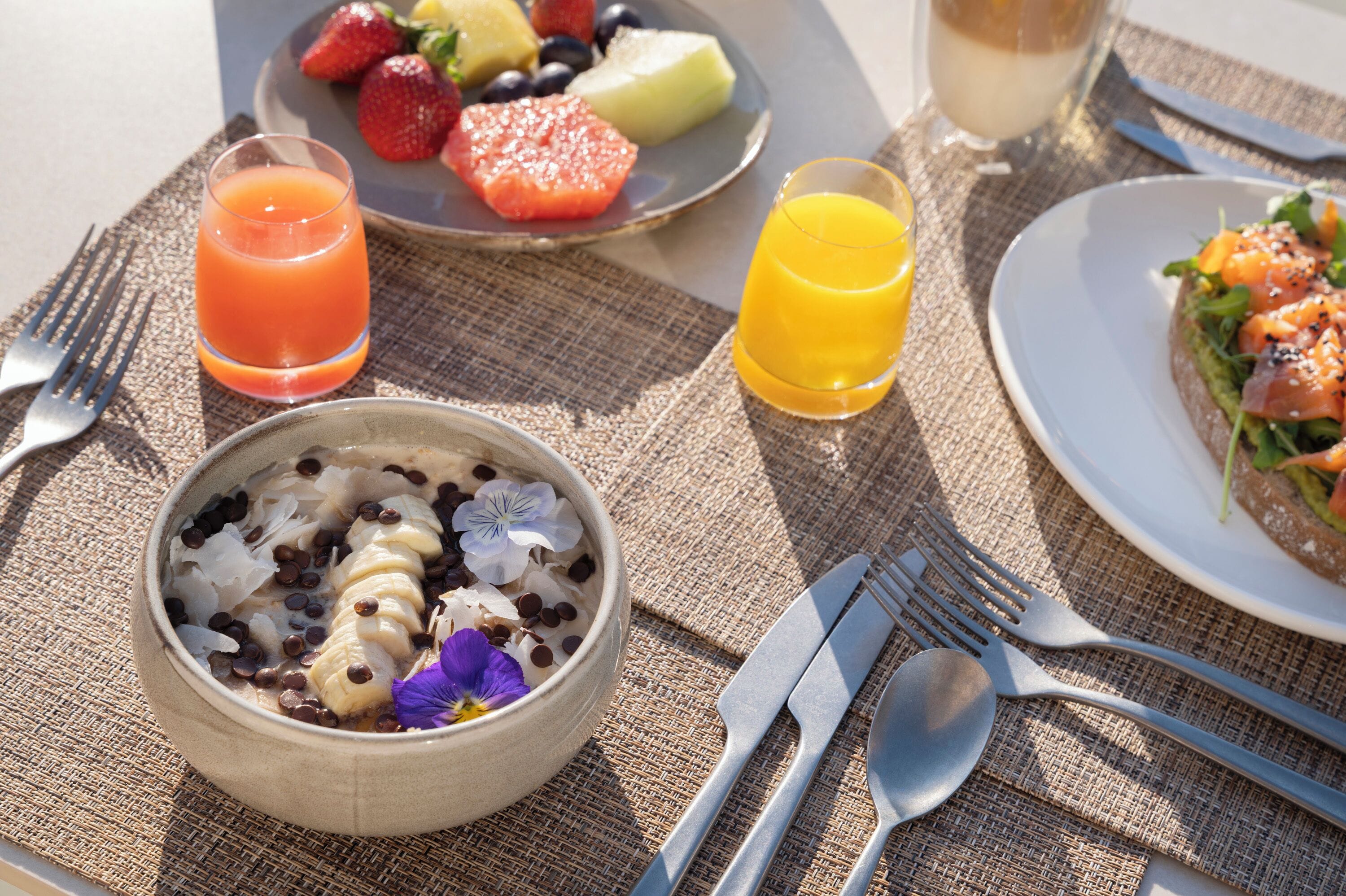 Un desayuno con un tazón de cereal, un plato de fruta y dos vasos de jugo.