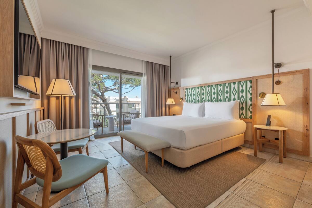 Habitación de hotel con cama, una mesita, una silla, un banco y vistas al exterior.