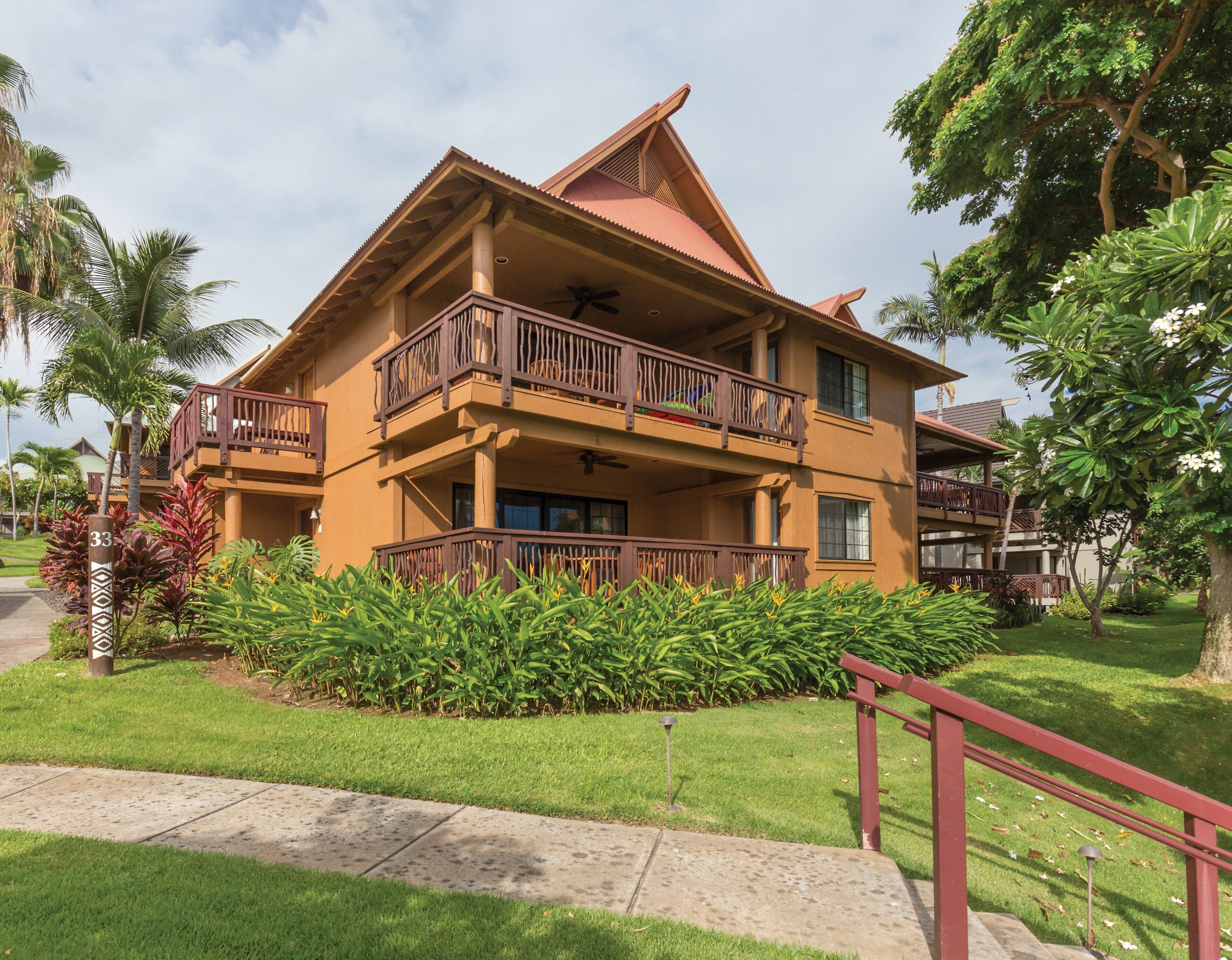 A two-story building with a balcony on the upper floor, surrounded by lush greenery.
