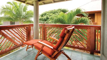 A wooden chair with a cushion on a balcony with a tiled floor, surrounded by a wooden railing and greenery.