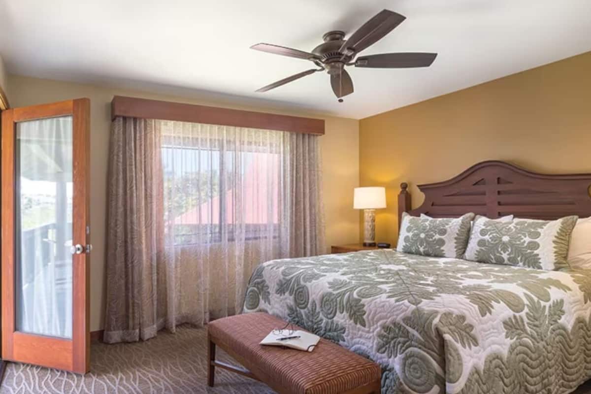 A hotel room with a bed, a desk, a chair, a ceiling fan, and a window with curtains.