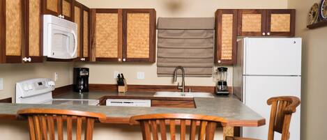 A kitchen with wooden cabinets, a microwave, a refrigerator, a sink, and a coffee maker. There are three wooden chairs around the kitchen island.