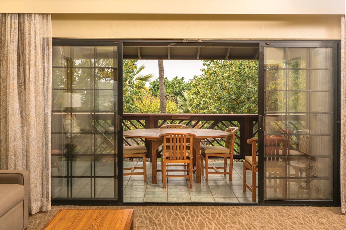A sliding glass door leading to an outdoor patio with a wooden table and chairs, a cushioned bench, and a view of greenery.