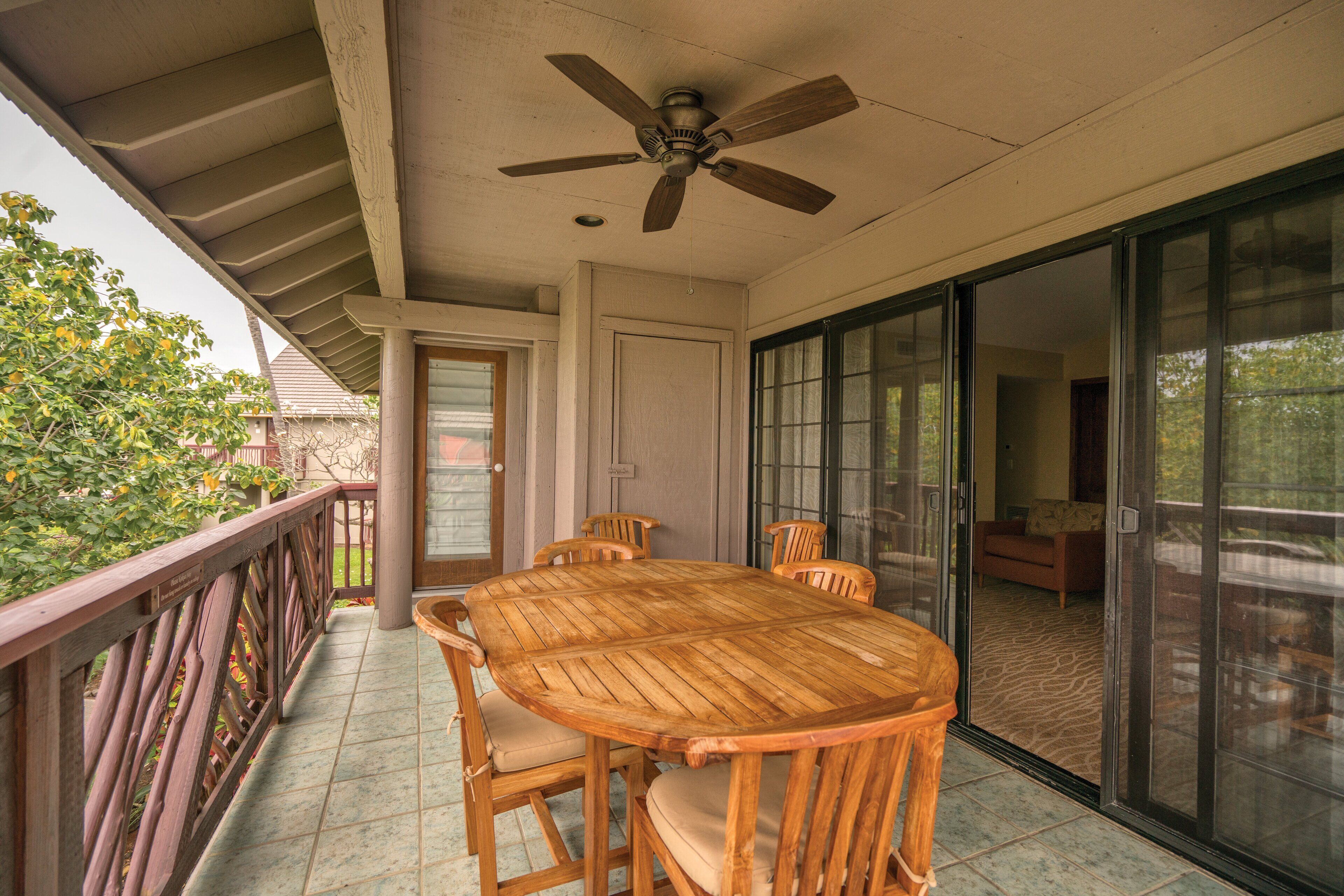 A covered patio with a wooden table and chairs, a ceiling fan, and a sliding glass door leading to an interior living area.