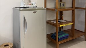 Une petite cuisine équipée d’un réfrigérateur en acier inoxydable, d’une machine à café et d’un petit panier. À côté se trouve une étagère en bois avec un porte-serviettes suspendu, un coffre-fort et un panneau indiquant qu’il est interdit d’emporter les serviettes de piscine hors de l’établissement.