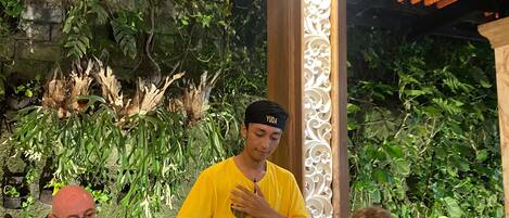 A restaurant with a table set for four people, a waiter in a yellow shirt, and a backdrop of green foliage.