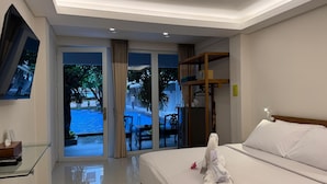 Une chambre d’hôtel équipée d’un lit, d’une télévision, d’une table en verre et offrant une vue sur une piscine et un espace extérieur.