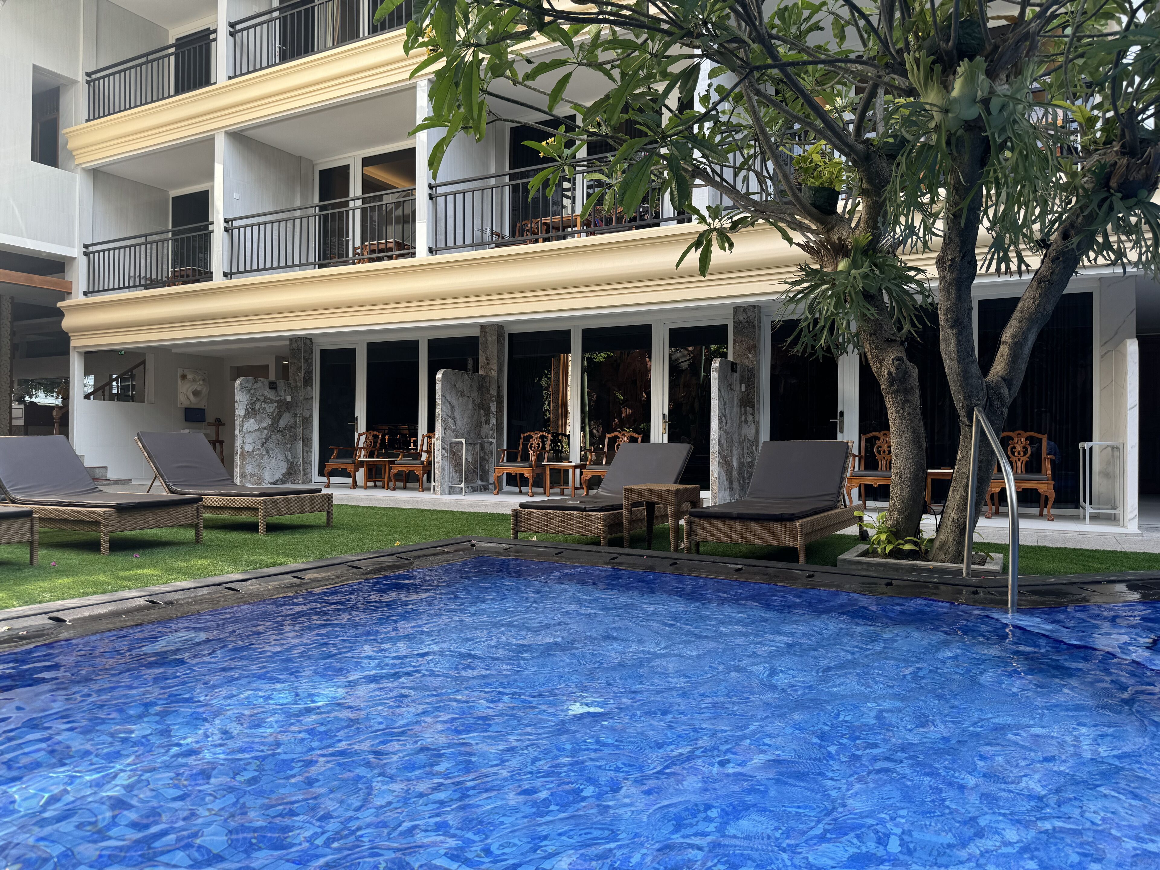 Zona de piscina con sillas de descanso y vistas a un edificio de varios pisos con balcones.