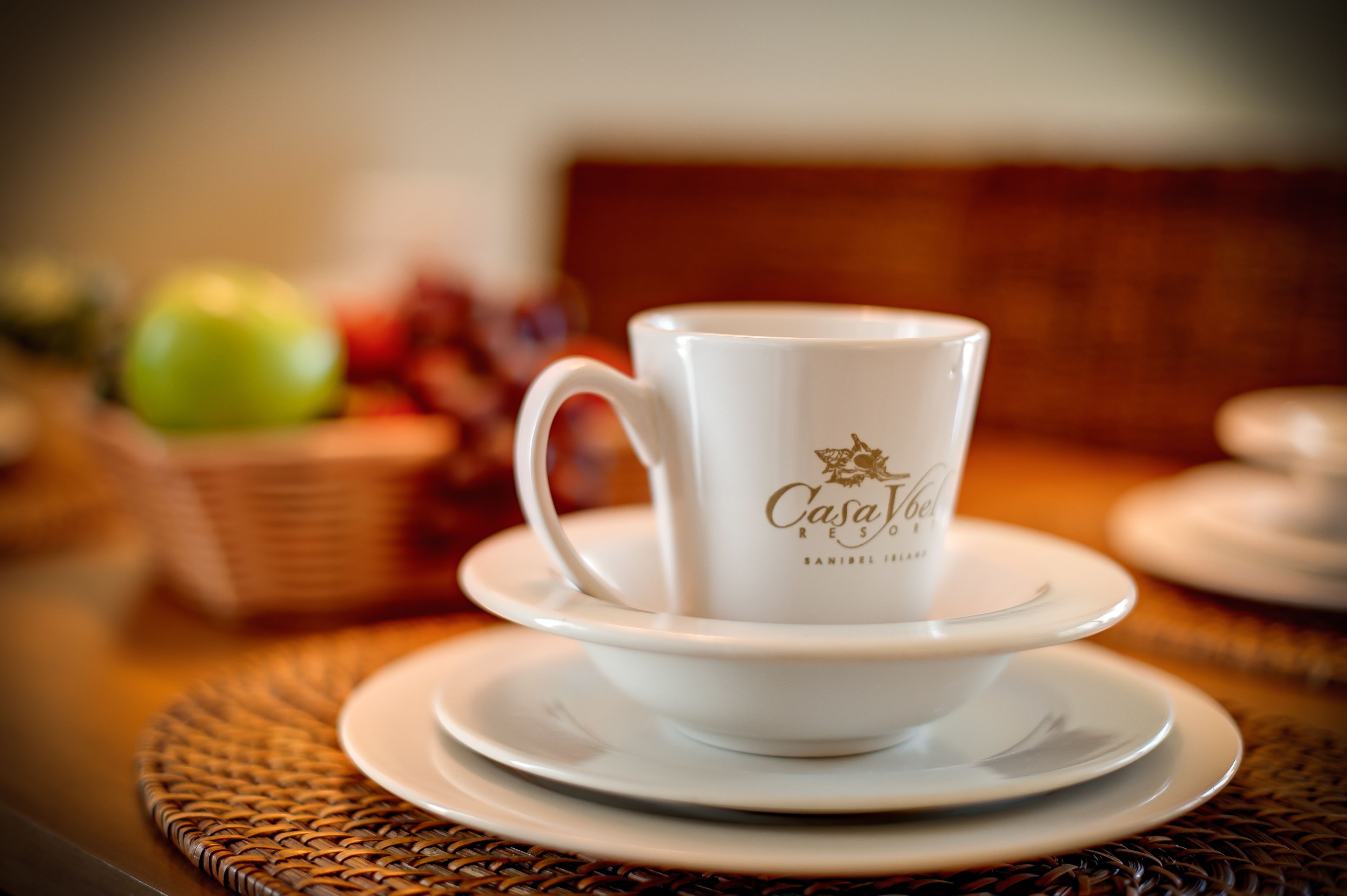 A white ceramic cup with "Casa Joven" text on a saucer, placed on a woven table mat.