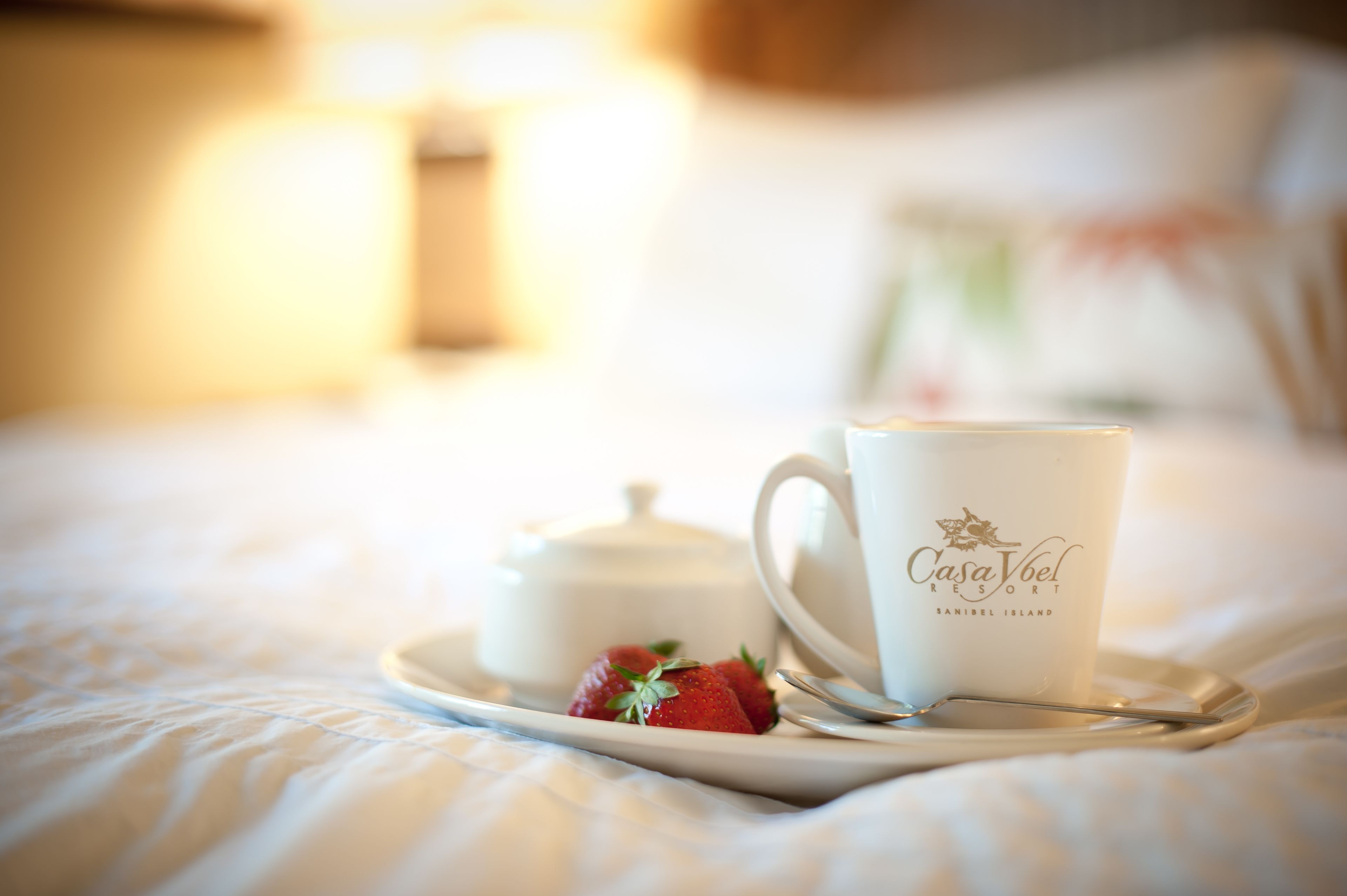 A tray with a white mug labeled "Casa Vbel Resort" and a teapot on a bed with white bedding.
