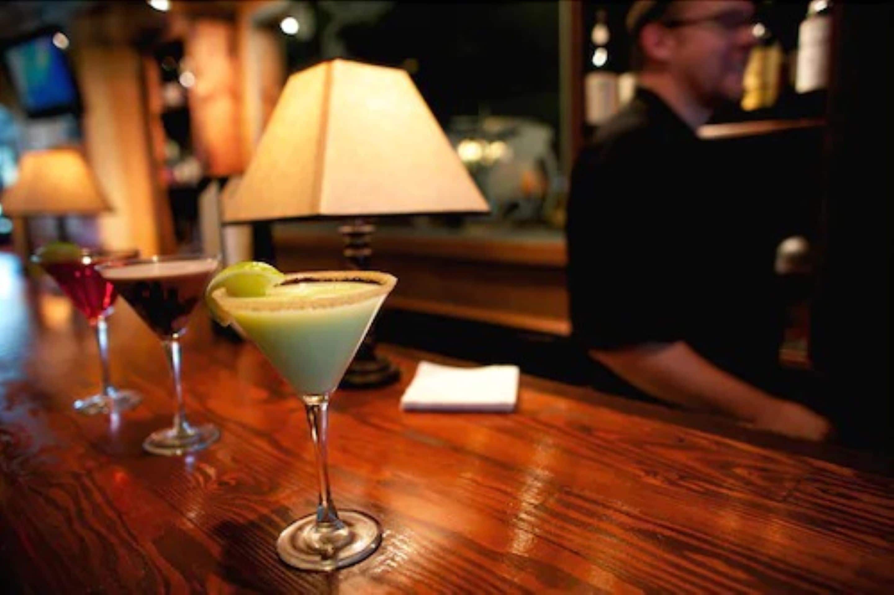 Un bar con una copa de martini, un cóctel adornado con lima y otro cóctel con espuma.