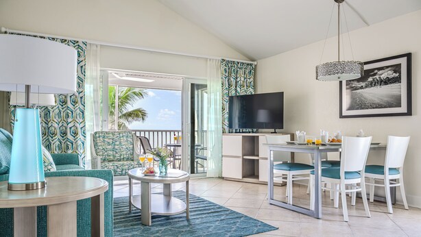 A modern living room with a TV, dining table, and chairs. There is a balcony with a view of palm trees. - Casa Ybel Resort (Sanibel)