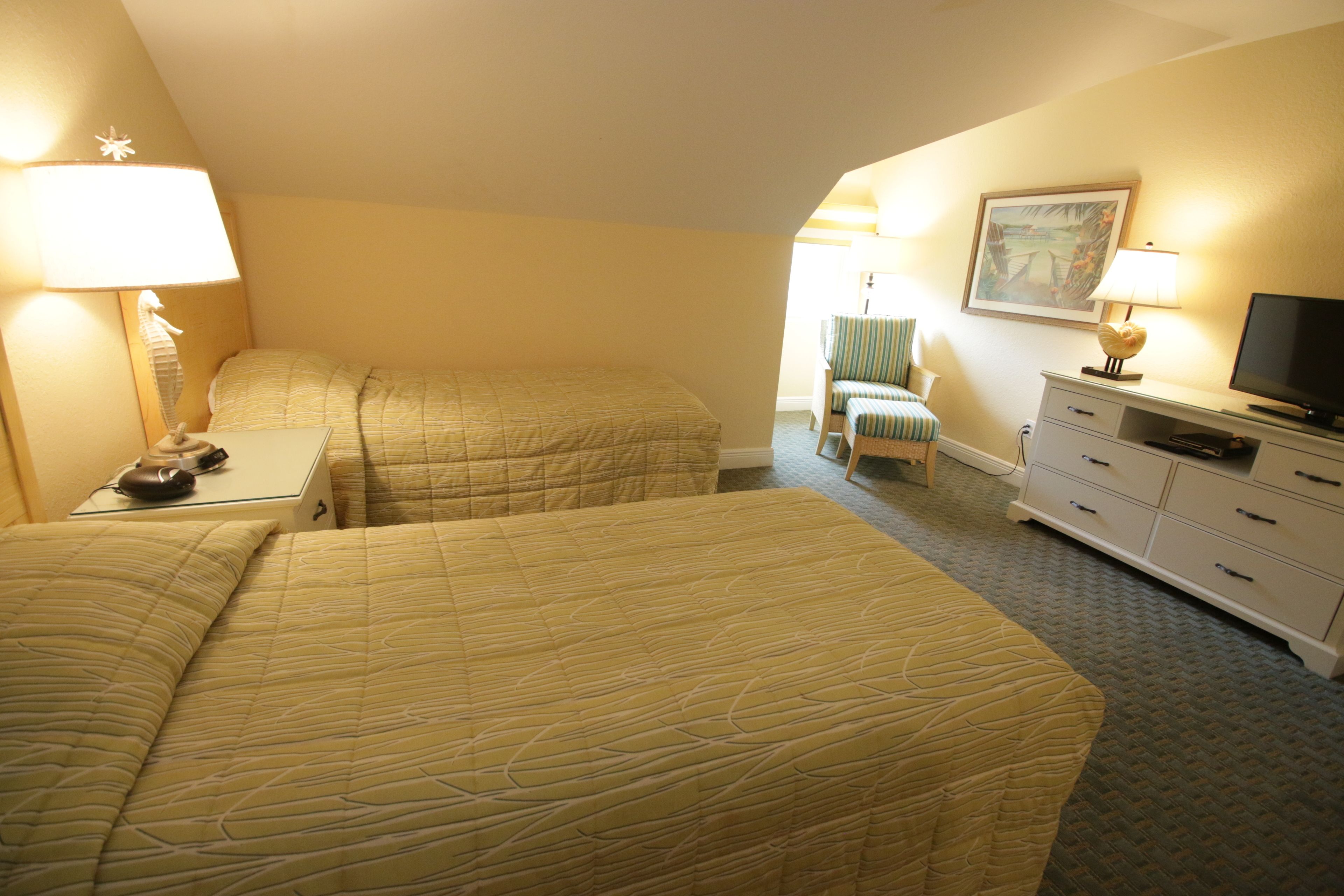 Une chambre d’hôtel avec deux lits, un bureau avec une lampe, une chaise, une commode et un téléviseur.