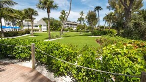 A well-maintained garden with a wooden deck, palm trees, and a building in the background. - Casa Ybel Resort (Sanibel)