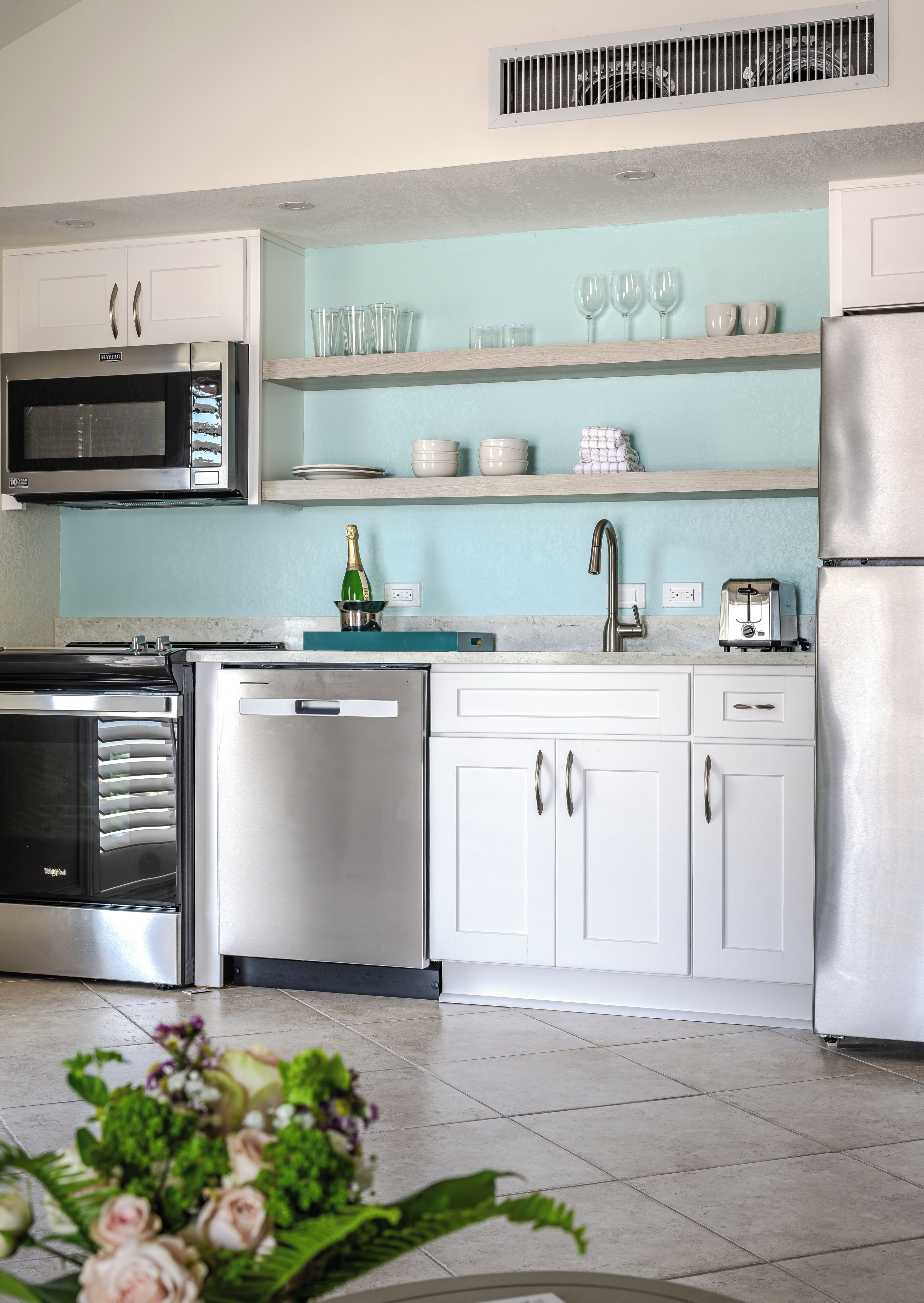 Una cocina moderna con electrodomésticos de acero inoxidable, armarios blancos y salpicadero azul claro.