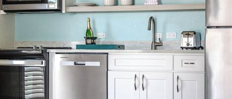 Una cocina moderna con electrodomésticos de acero inoxidable, armarios blancos y salpicadero azul claro.